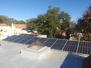 Rooftop with multiple solar panels in a residential area surrounded by trees and neighboring houses.