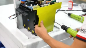Technician assembling a solar inverter using a screwdriver, securing a yellow panel onto the inverter's structure.