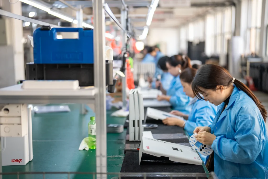 Industrial assembly line where workers in blue uniforms are assembling SAKO solar inverters, emphasizing renewable energy production.
