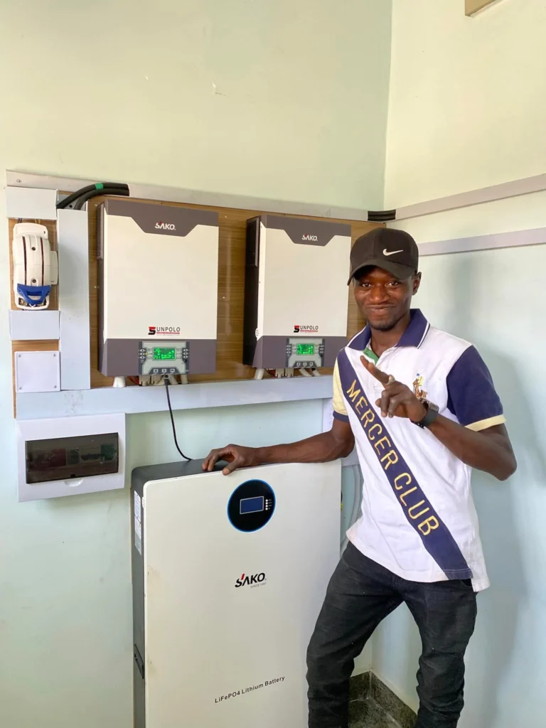 Man standing next to SAKO energy storage system with inverters and lithium battery on wall.