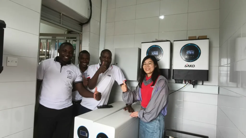 Technicians giving thumbs up in front of a SAKO energy storage installation, featuring wall-mounted solar inverters and a rectangular energy unit.