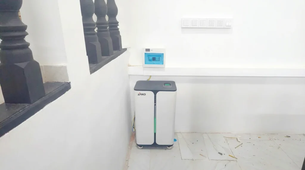SAKO energy storage unit placed in the corner of a bright room with a white tiled floor and electrical box above.