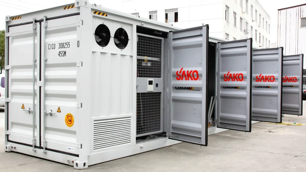 Several containerized SAKO energy storage systems with open doors, displaying the brand logo, in a factory yard setting.
