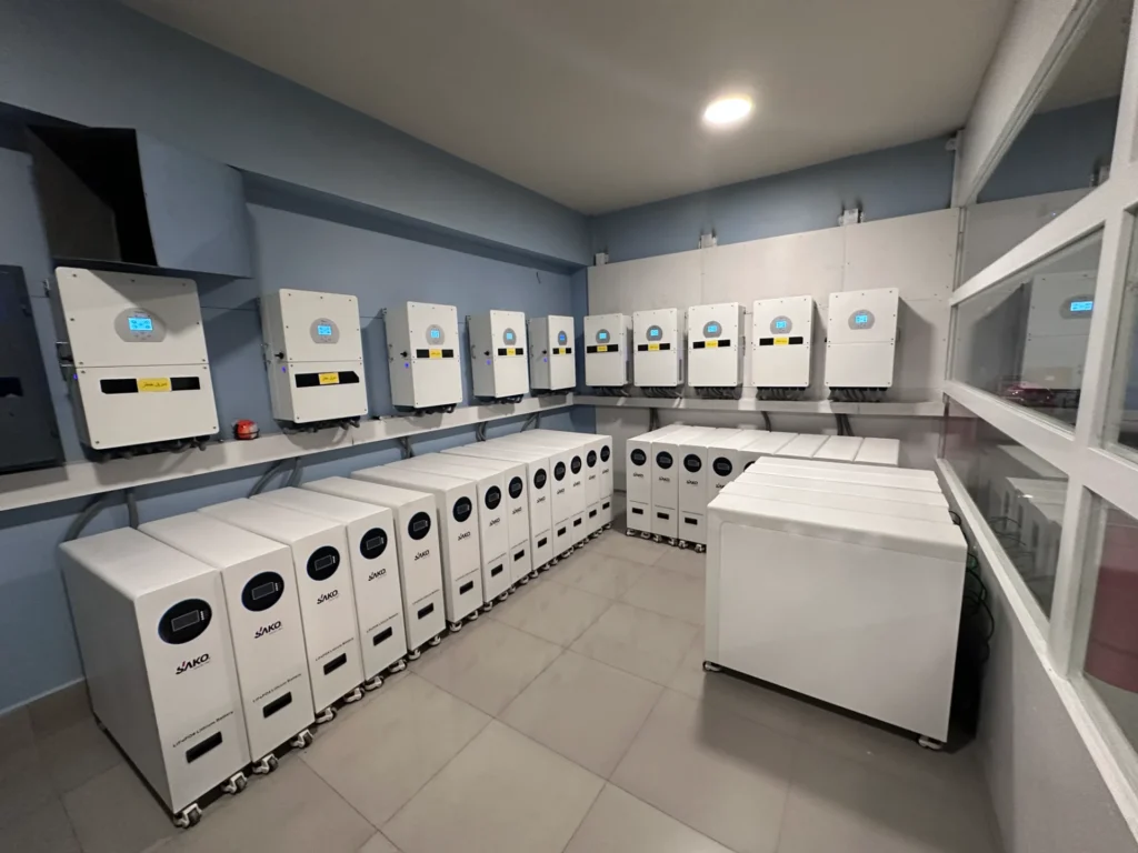 Room with SAKO energy storage lithium batteries and solar inverters lined up systematically along walls.