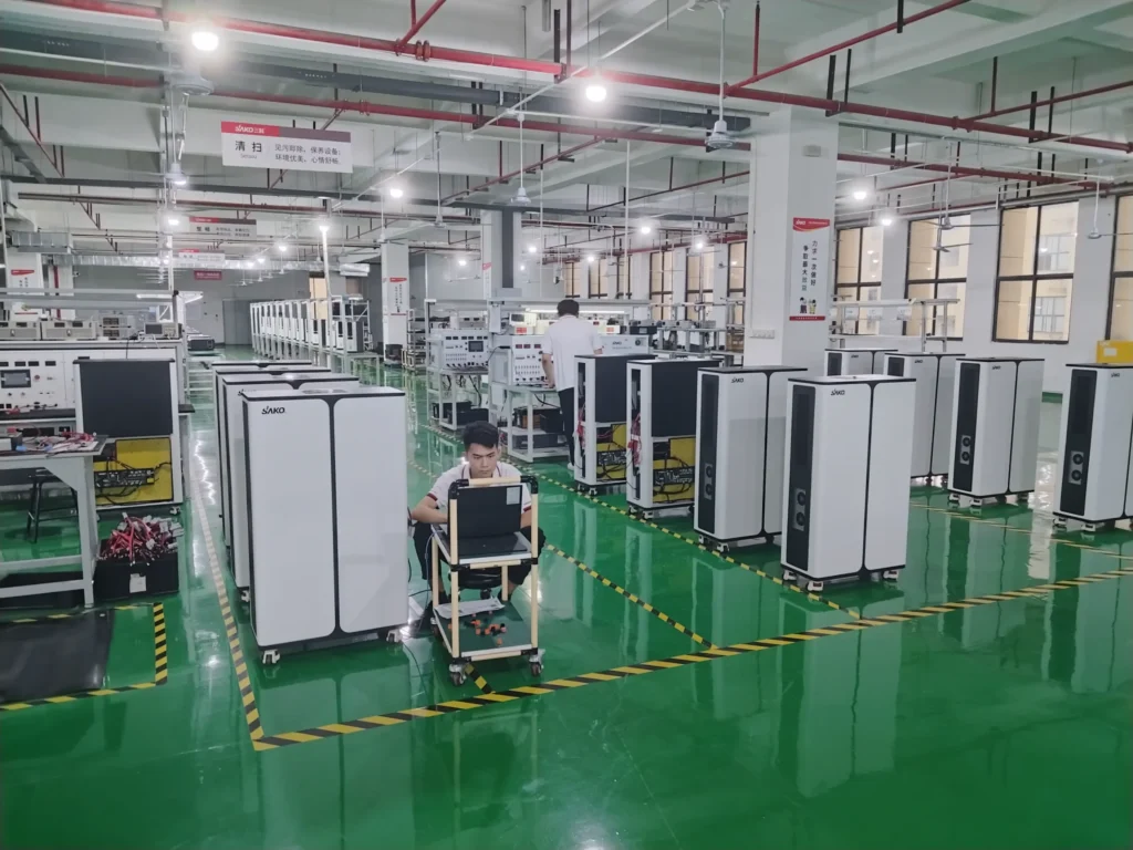 SAKO-branded energy storage systems lined up in modern factory setting with individuals working on production tasks.