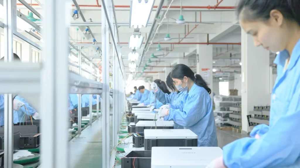 Workers in blue lab coats handle power conversion products on an assembly line at the SAKO Tedepe factory.