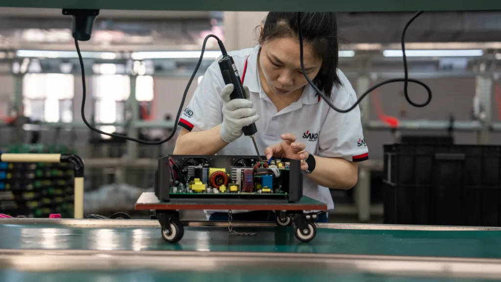 Factory worker assembling a solar inverter circuit board at SAKO's Tedepe manufacturing base, wearing a branded uniform.
