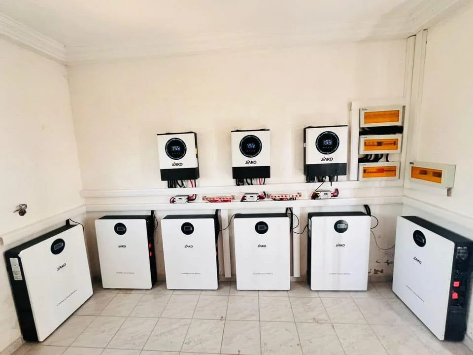 SAKO solar inverters mounted on a wall above several energy storage lithium batteries in a clean indoor setup.