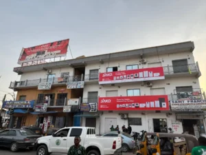 Three-story building displaying SAKO brand banners indicating energy product offerings; vehicles in foreground.