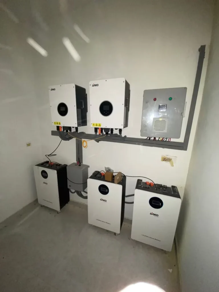 SAKO branded solar inverters mounted on a wall above three energy storage lithium batteries in a clean room setting.