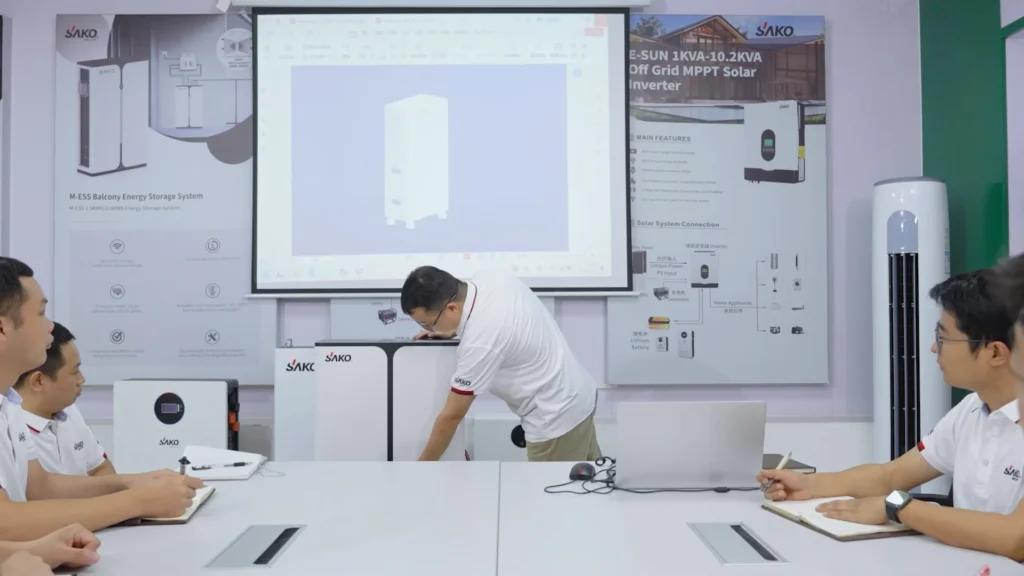 SAKO team members in a meeting room discussing energy storage solutions with a presentation screen and product posters.