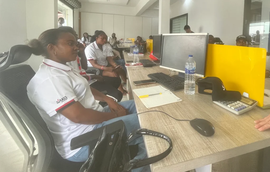 SAKO team members in an office setting with computers and notes, engaged in a discussion or training session.