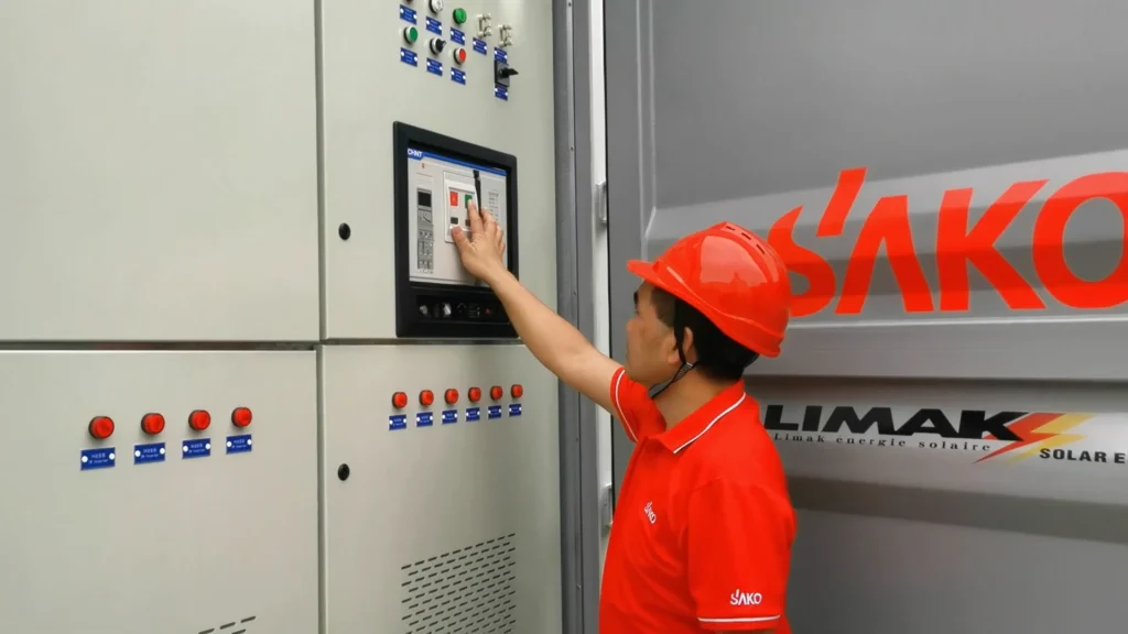 SAKO technician in a red uniform and helmet interacting with a control panel in a manufacturing setup, showcasing brand involvement.