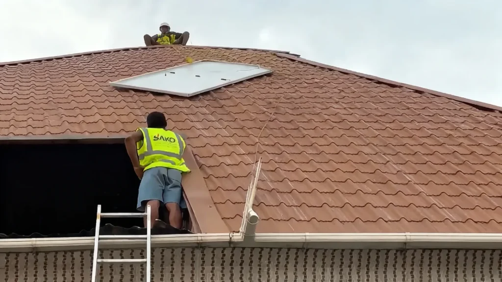 SAKO worker in high-visibility vest installing a solar panel on a tiled brown rooftop, using a ladder for access and safety equipment.