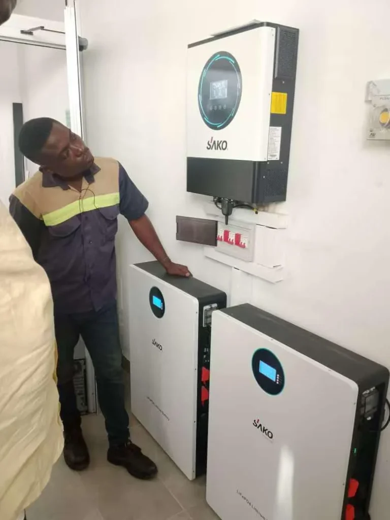 Technician examining SAKO energy storage system with inverters and lithium batteries installed on a wall.