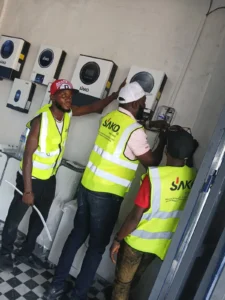 Three technicians in high-visibility vests installing SAKO solar inverters on a wall.