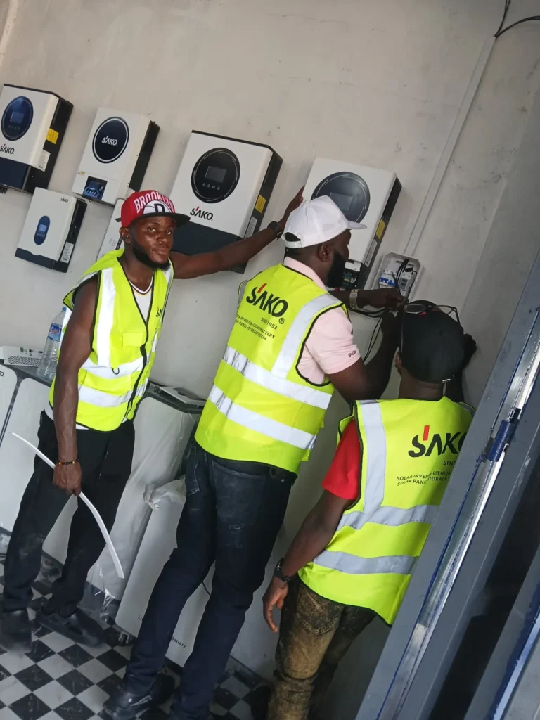 Three technicians in high-visibility vests installing SAKO solar inverters on a wall.
